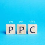 Tres bloques de madera con la palabra "PPC" escritos en ellos están dispuestos uno al lado del otro, cada uno coronado con las palabras "pagar", "por" y "clic", que simbolizan campañas de publicidad efectivas sobre un fondo azul.