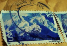 Primer plano de dos sellos postales de EE. UU. que muestran el monte McKinley en Alaska, parcialmente oscurecidos por un matasellos de Nueva York, resaltando íconos perdurables incluso en la era del comercio electrónico.