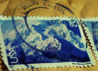 Primer plano de dos sellos postales de EE. UU. que muestran el monte McKinley en Alaska, parcialmente oscurecidos por un matasellos de Nueva York, resaltando &iacute;conos perdurables incluso en la era del comercio electr&oacute;nico.