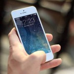 Mano sosteniendo un teléfono inteligente blanco que muestra la pantalla de bloqueo con la hora 12:23 del lunes 29 de julio.