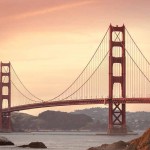 Puente Golden Gate al atardecer, cruzando la bahía con colinas al fondo y una costa rocosa en primer plano.