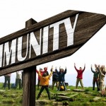 Cartel de madera con el texto "COMUNIDAD", que señala a un grupo de personas que levantan los brazos en un entorno al aire libre con césped.