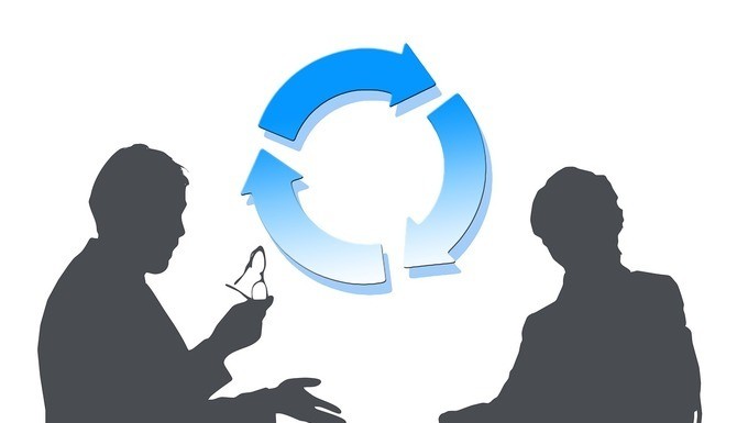 Dos personas en silueta están sentadas una frente a la otra. Una de ellas hace gestos mientras sostiene unas copas. Entre ellas se muestra un diagrama de flechas circulares.