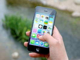 Una mano sostiene un teléfono inteligente que muestra varios íconos de aplicaciones, haciendo alusión al vasto mercado de tecnologías digitales, frente a un fondo exterior borroso.