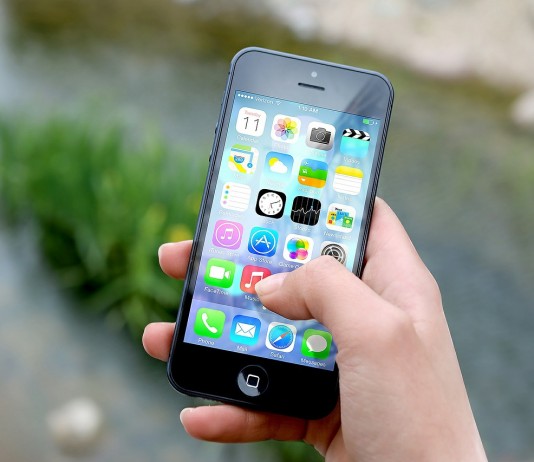 Una mano sostiene un teléfono inteligente que muestra varios íconos de aplicaciones, haciendo alusión al vasto mercado de tecnologías digitales, frente a un fondo exterior borroso.