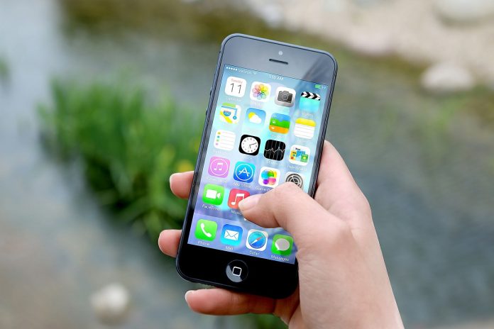 Posicionar tu aplicación te garantizará mayores descargas Una mano sostiene un teléfono inteligente que muestra varios íconos de aplicaciones, haciendo alusión al vasto mercado de tecnologías digitales, frente a un fondo exterior borroso.