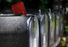 Primer plano de una fila de buzones negros con una bandera roja levantada, señalando la recogida de comunicaciones importantes, como boletines informativos.