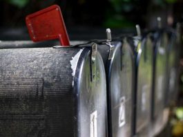 Primer plano de una fila de buzones negros con una bandera roja levantada, señalando la recogida de comunicaciones importantes, como boletines informativos.