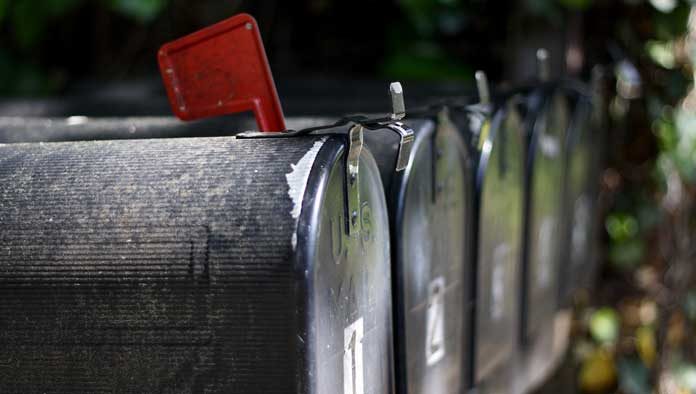 Primer plano de una fila de buzones negros con una bandera roja levantada, señalando la recogida de comunicaciones importantes, como boletines informativos.