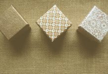 Tres cajas de regalo con patrones texturizados están dispuestas en fila sobre una superficie de arpillera, listas para deleitar a sus clientes.