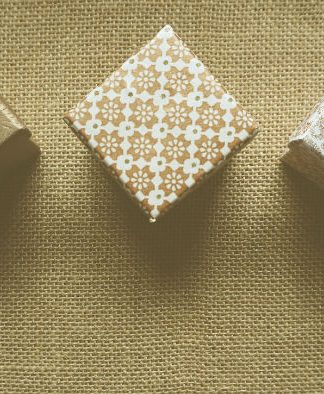 Tres cajas de regalo con patrones texturizados están dispuestas en fila sobre una superficie de arpillera, listas para deleitar a sus clientes.