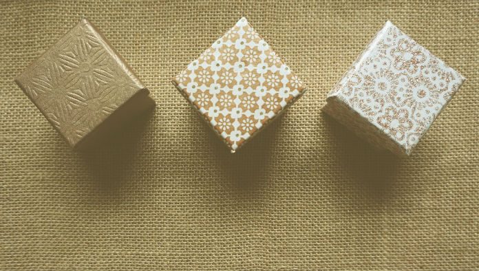 Regalo-promo Tres cajas de regalo con patrones texturizados están dispuestas en fila sobre una superficie de arpillera, listas para deleitar a sus clientes.