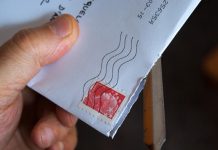 Una mano que utiliza hábilmente un abrecartas de metal para revelar el contenido de un sobre blanco con un sello postal rojo; todo es parte de una apertura ingeniosa, dominada por especialistas en marketing para lograr una primera impresión perfecta.