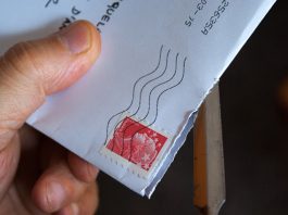 Una mano que utiliza hábilmente un abrecartas de metal para revelar el contenido de un sobre blanco con un sello postal rojo; todo es parte de una apertura ingeniosa, dominada por especialistas en marketing para lograr una primera impresión perfecta.