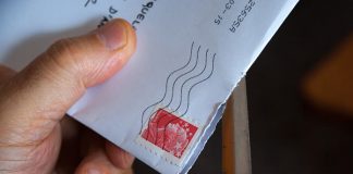 Una mano que utiliza hábilmente un abrecartas de metal para revelar el contenido de un sobre blanco con un sello postal rojo; todo es parte de una apertura ingeniosa, dominada por especialistas en marketing para lograr una primera impresión perfecta.