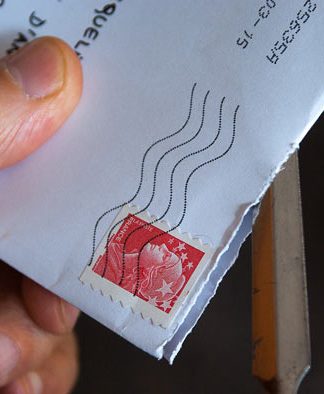 Una mano que utiliza hábilmente un abrecartas de metal para revelar el contenido de un sobre blanco con un sello postal rojo; todo es parte de una apertura ingeniosa, dominada por especialistas en marketing para lograr una primera impresión perfecta.