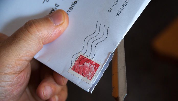 Una mano que utiliza hábilmente un abrecartas de metal para revelar el contenido de un sobre blanco con un sello postal rojo; todo es parte de una apertura ingeniosa, dominada por especialistas en marketing para lograr una primera impresión perfecta.