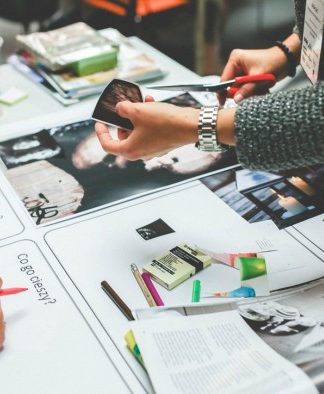 Personas colaborando en una mesa llena de papeles, fotos, marcadores y revistas, intercambiando ideas para un nuevo logotipo de empresa que se destaque de la competencia.