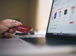 Una persona sostiene una tarjeta de crédito frente a una computadora portátil, navegando por un sitio web de compras en línea que muestra las últimas tendencias y descuentos exclusivos en comercio electrónico.