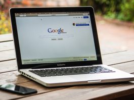 Una computadora portátil que muestra la página de inicio de Google descansa sobre una mesa de madera junto a un teléfono inteligente, encarnando una de las 7 estrategias para impulsar el SEO y atraer más usuarios.