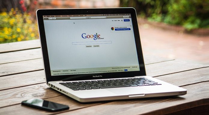 7 estrategias SEO Actuales para tu negocio Una computadora portátil que muestra la página de inicio de Google descansa sobre una mesa de madera junto a un teléfono inteligente, encarnando una de las 7 estrategias para impulsar el SEO y atraer más usuarios.