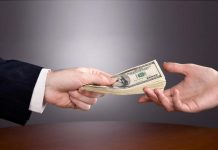 Una mano de traje ofrece una pila de billetes de dólar a otra, simbolizando el inicio de un nuevo negocio sobre la mesa de planificación.