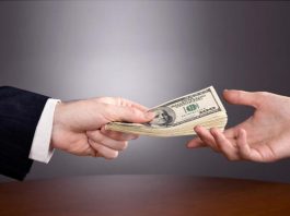 Una mano de traje ofrece una pila de billetes de dólar a otra, simbolizando el inicio de un nuevo negocio sobre la mesa de planificación.
