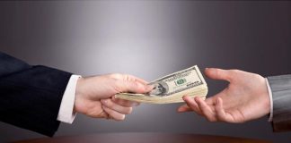Una mano de traje ofrece una pila de billetes de dólar a otra, simbolizando el inicio de un nuevo negocio sobre la mesa de planificación.