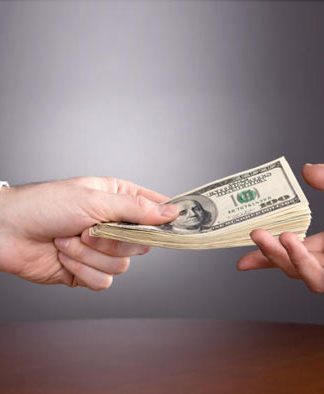 Préstamos personales: una opción para arrancar tu negocio Una mano de traje ofrece una pila de billetes de dólar a otra, simbolizando el inicio de un nuevo negocio sobre la mesa de planificación.