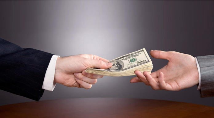 Préstamos personales: una opción para arrancar tu negocio Una mano de traje ofrece una pila de billetes de dólar a otra, simbolizando el inicio de un nuevo negocio sobre la mesa de planificación.