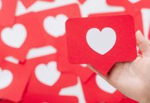 Una mano sostiene una tarjeta roja con un corazón blanco, que se asemeja a un ícono de las redes sociales, en medio de un fondo de tarjetas similares, perfecto para ilustrar tácticas de participación en las redes sociales.