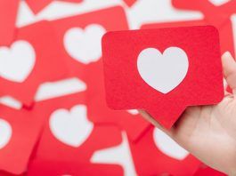 Una mano sostiene una tarjeta roja con un corazón blanco, que se asemeja a un ícono de las redes sociales, en medio de un fondo de tarjetas similares, perfecto para ilustrar tácticas de participación en las redes sociales.