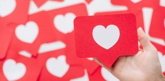 Una mano sostiene una tarjeta roja con un corazón blanco, que se asemeja a un ícono de las redes sociales, en medio de un fondo de tarjetas similares, perfecto para ilustrar tácticas de participación en las redes sociales.