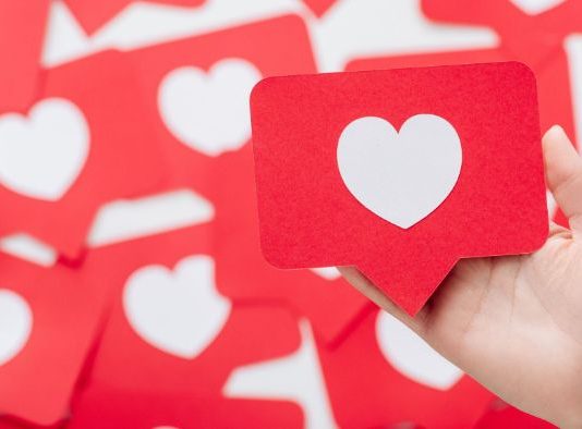 Una mano sostiene una tarjeta roja con un corazón blanco, que se asemeja a un ícono de las redes sociales, en medio de un fondo de tarjetas similares, perfecto para ilustrar tácticas de participación en las redes sociales.