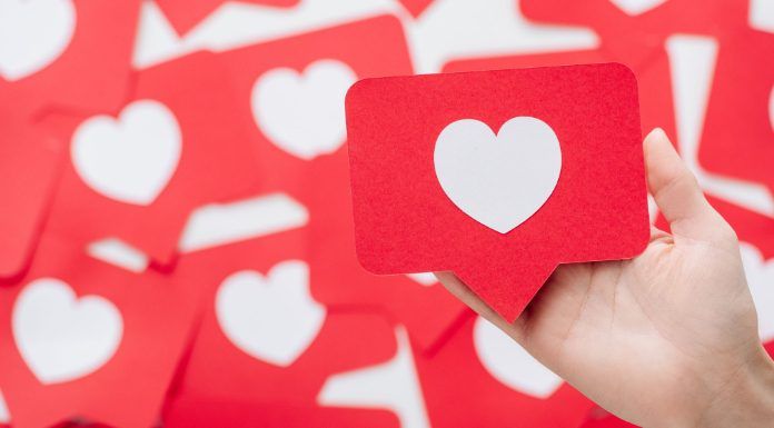 Las mejores tácticas para fomentar el engagement en redes sociales Una mano sostiene una tarjeta roja con un corazón blanco, que se asemeja a un ícono de las redes sociales, en medio de un fondo de tarjetas similares, perfecto para ilustrar tácticas de participación en las redes sociales.