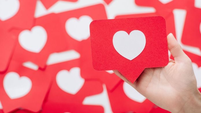 Una mano sostiene una tarjeta roja con un corazón blanco, que se asemeja a un ícono de las redes sociales, en medio de un fondo de tarjetas similares, perfecto para ilustrar tácticas de participación en las redes sociales.