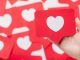 Las mejores tácticas para fomentar el engagement en redes sociales Una mano sostiene una tarjeta roja con un corazón blanco, que se asemeja a un ícono de las redes sociales, en medio de un fondo de tarjetas similares, perfecto para ilustrar tácticas de participación en las redes sociales.