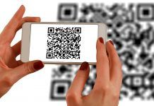 Una persona escanea un código QR con un teléfono inteligente, frente a un código QR más grande que aparece como fondo borroso, fusionando a la perfección los ámbitos de la interacción fuera de línea con las estrategias de marketing digital.
