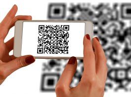 Una persona escanea un código QR con un teléfono inteligente, frente a un código QR más grande que aparece como fondo borroso, fusionando a la perfección los ámbitos de la interacción fuera de línea con las estrategias de marketing digital.