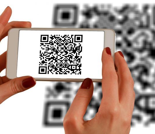 Una persona escanea un código QR con un teléfono inteligente, frente a un código QR más grande que aparece como fondo borroso, fusionando a la perfección los ámbitos de la interacción fuera de línea con las estrategias de marketing digital.