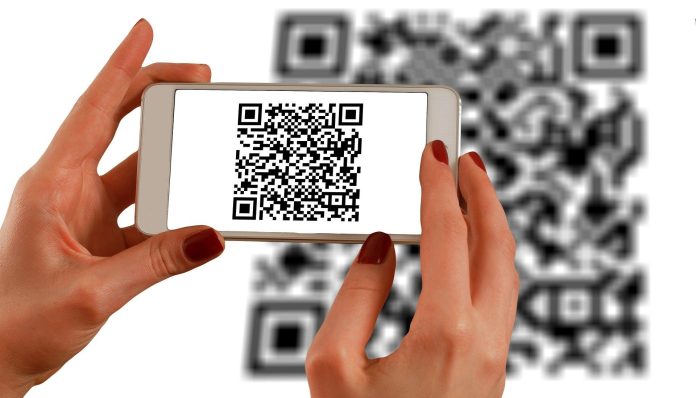 hands-1167612_1920 Una persona escanea un código QR con un teléfono inteligente, frente a un código QR más grande que aparece como fondo borroso, fusionando a la perfección los ámbitos de la interacción fuera de línea con las estrategias de marketing digital.