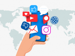 Una mano que sostiene un teléfono inteligente con varios íconos de redes sociales flotando sobre él. De fondo, un mapa del mundo.